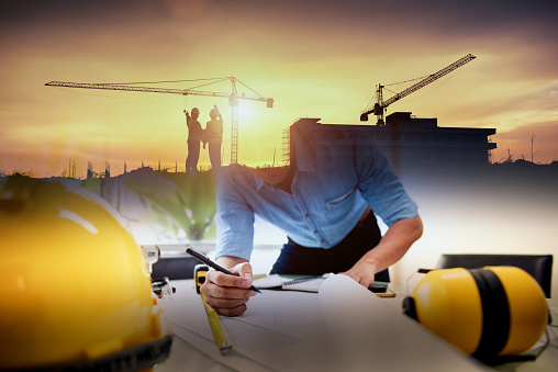 Project manager reviewing plans construction cranes at sunset — APF greenfields development South Africa